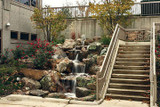 Natural stone waterfall cascading over multiple landscaped rock tiers beside an outdoor staircase