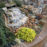 Small curved corner waterfall installed in landscaping beside a brick wall
