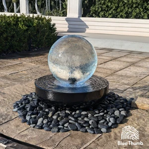 14-inch Crystal Sphere Fountain flowing over a black steel bowl surrounded by polished black pebbles