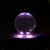 14-inch crystal sphere lit in purple - A glowing transparent acrylic crystal sphere fountain emits soft purple light in the darkness, creating a mystical and tranquil atmosphere in a garden setting.