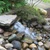 Compact rock-lined waterfall cascading into a gravel bed beside landscape plants