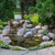 Small backyard garden pond with a rock waterfall, orange fish, boulders, and lush landscaping.