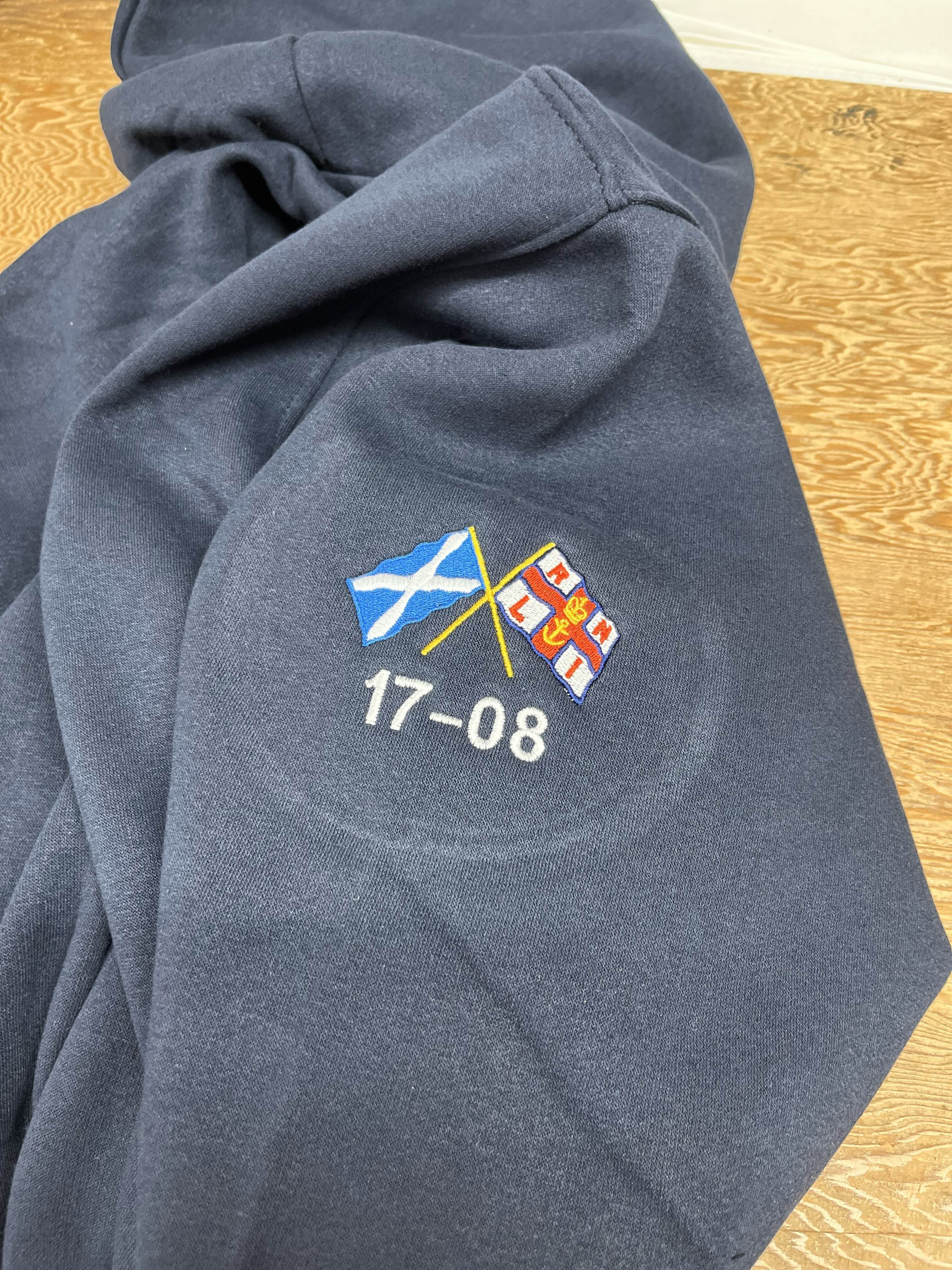 Logo embroidered on the right hand sleeve of a Navy Hooded Sweatshirt