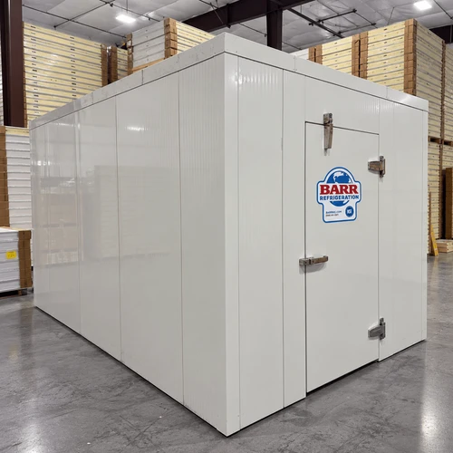 White walk-in cooler unit with closed hinged door, featuring insulated panel walls front right view