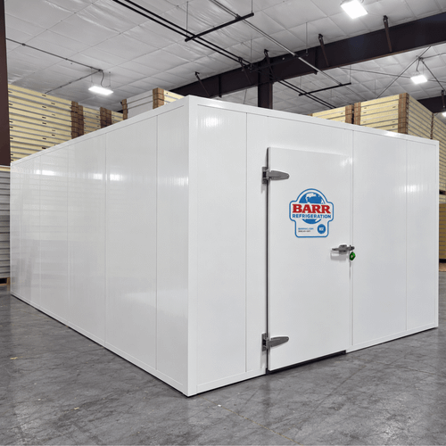 White walk-in cooler unit with closed hinged door, featuring insulated panel walls and a stack of ceiling panels
