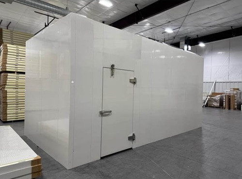 White walk-in cooler unit with closed hinged door, featuring insulated panel walls and a stack of ceiling panels