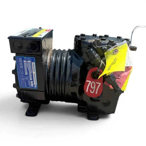 Front-right view of a used Copeland KAJA-011E-TAC 1 HP compressor (3 phase 208-230 volt), a semi-hermetic reciprocating compressor with a red inventory tag "797" and a yellow "ADD OIL TO COMPRESSOR" tag with an attached red caution tag hanging from the valve plate.