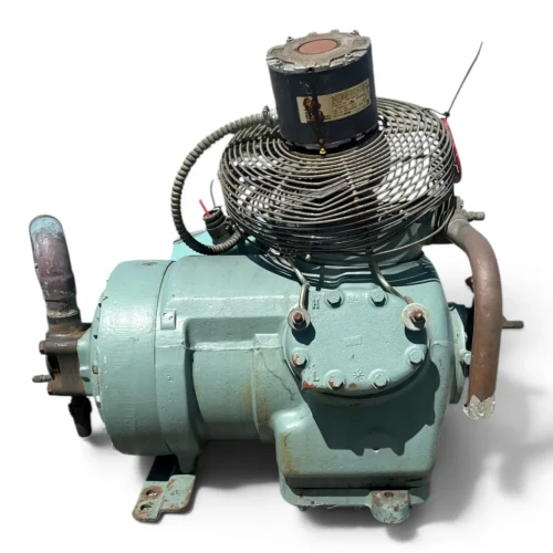 Close three-quarter view of the used Carlyle 06DM3376DC3650 10 HP compressor (3 phase 460 volt), aqua-green housing with a red round inventory tag hanging near the top, a copper refrigerant line bending across the front, and a cluster of valves and fittings at the lower right.
