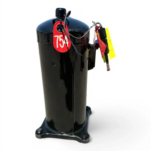 Front-right angled view of a used Copeland 9RC1-101A-TFD 10 HP compressor, 3 phase 460 volt, showing a yellow "Add Oil To Compressor" tag and a foil-wrapped tag hanging from a coiled wire at the top, the black terminal box, a blue Copeland Scroll rating nameplate, and two brass service valve stubs on the front face above the cast mounting base.