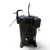 Front-left view of the used Copeland CRM3-0400-PFV 4 HP compressor (1 phase, 208-230 volt), a black cylindrical tank-style unit with two bent copper process stubs at the top (one foil-capped), a dark terminal box with hanging black wires on the right, a rusty weld seam around the mid-body, and a gray tripod base.