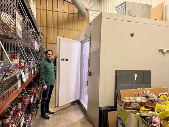 A food bank volunteer standing beside a walk-in cooler