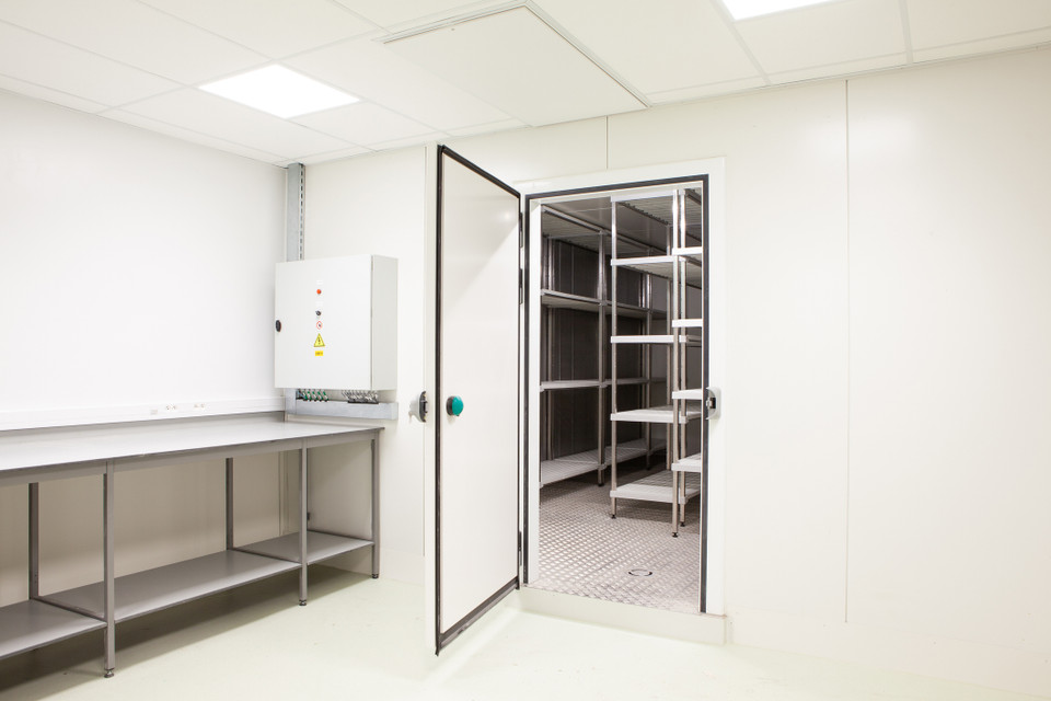 A commercial kitchen prep area beside an open walk-in cooler with storage shelving