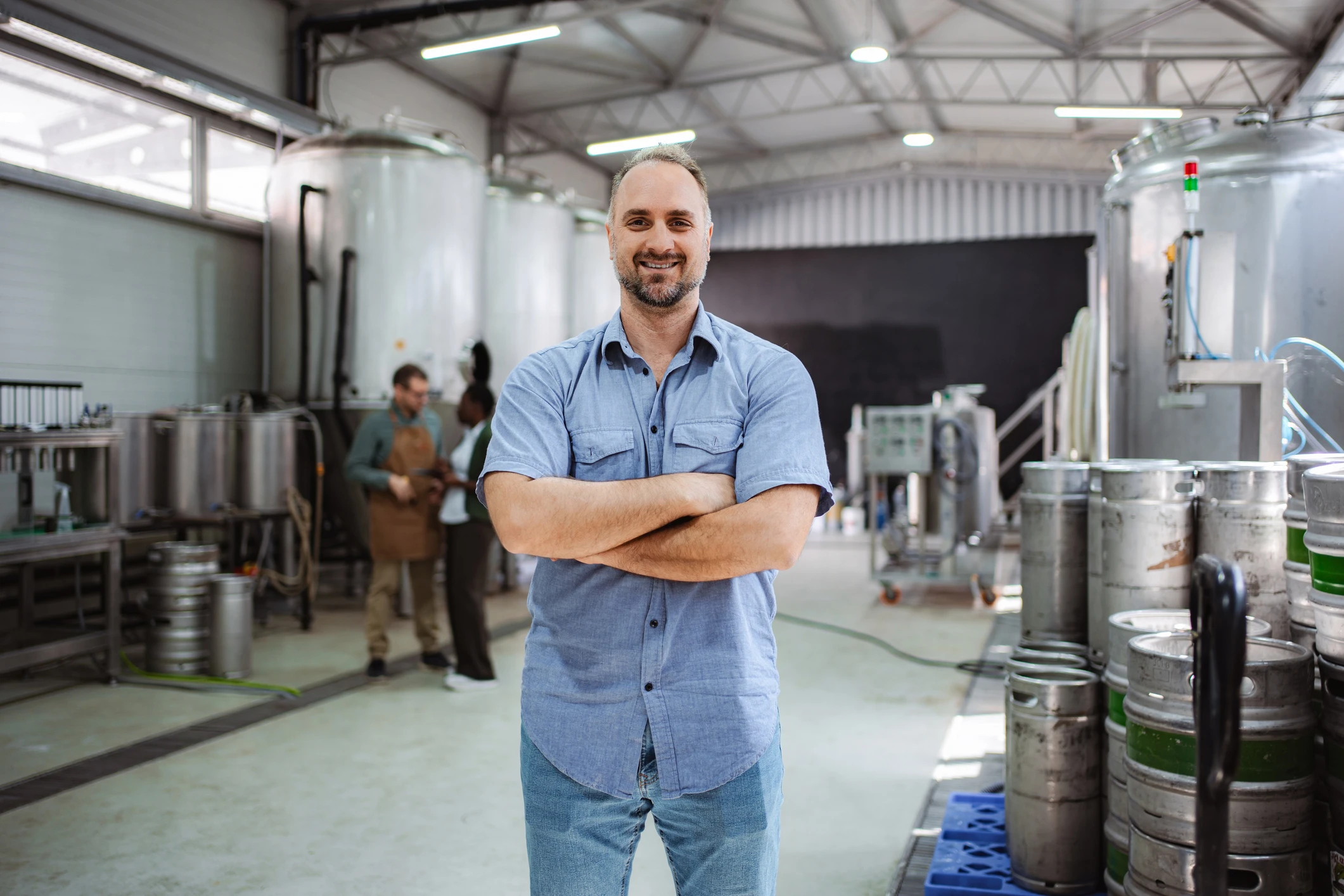 Brewery owner standing among stainless steel brewing tanks and kegs