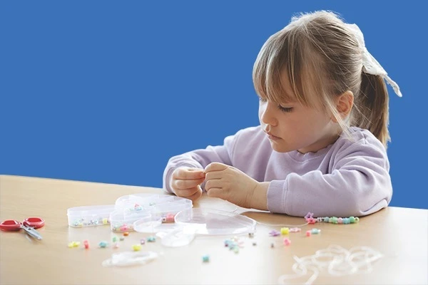 Young girl threading colourful beads onto string at a classroom table