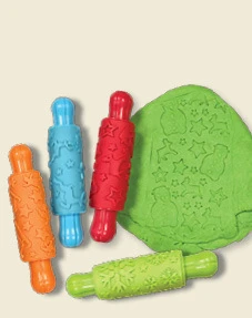 Four colourful patterned rolling pins beside green dough printed with festive shapes