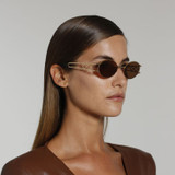 Side view of model wearing sunglasses | Oval sunglasses with brown lenses and gold frames | Metal | Carrie | Women's sunglasses | Karen Wazen Eyewear