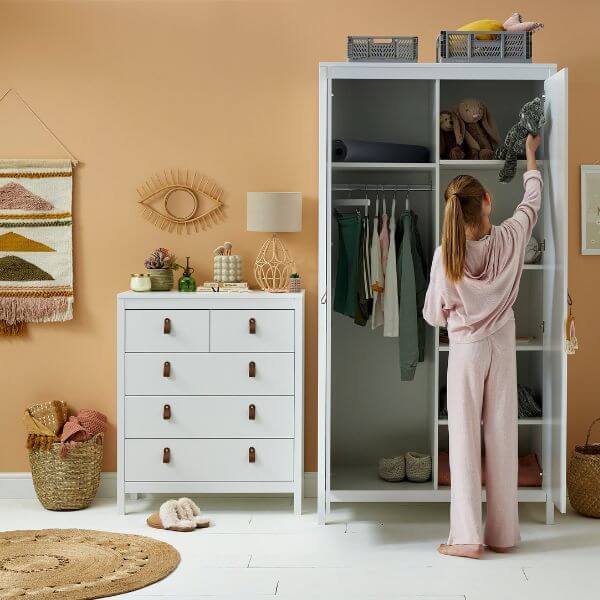 Girl taking a teddy bear out of a white wardrobe.