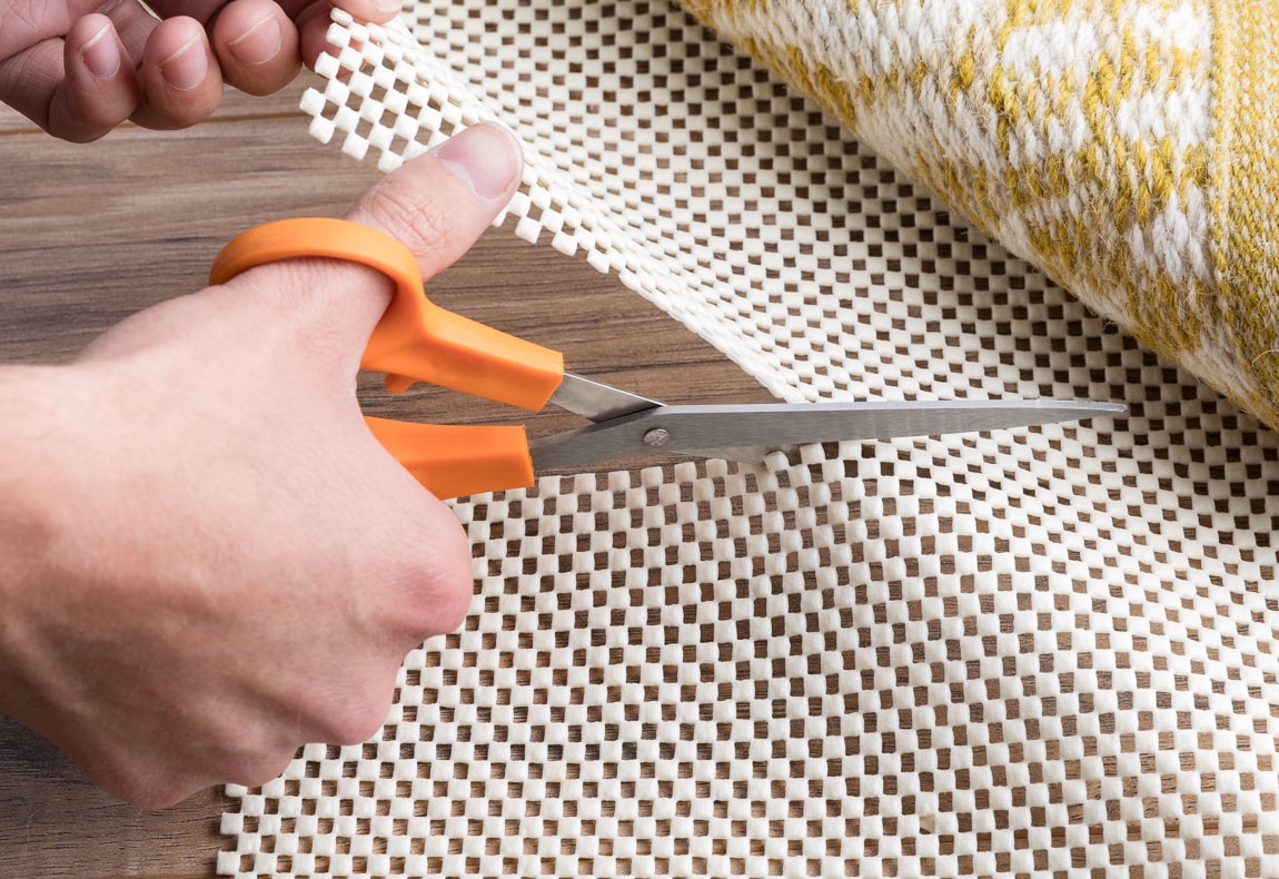 a person's hands using scissors to trim the rug pad