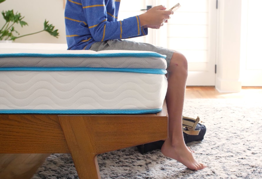 Boy sitting on the edge of the Linenspa 8" Memory Foam and Innerspring Hybrid Mattress