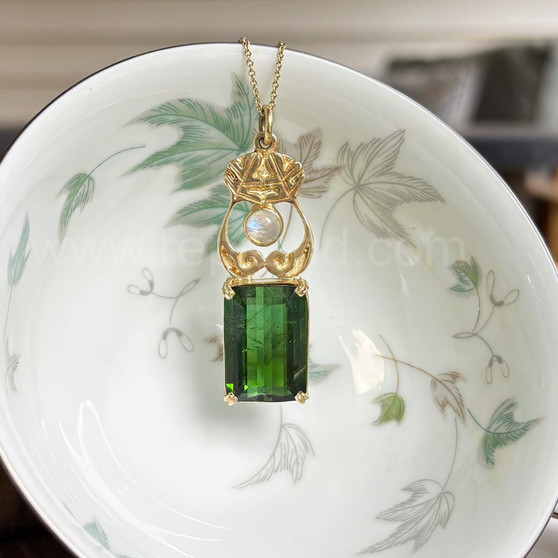 14kt yellow gold pendant with leaves and curls above a 20.71ct Green Tourmaline and accented with a Rainbow Moonstone. 