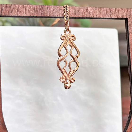 The Fadó Knot Pendant is formed from two overlapping heart shapes with curled ends and large bead accents at the bottom. Shown in rose gold.