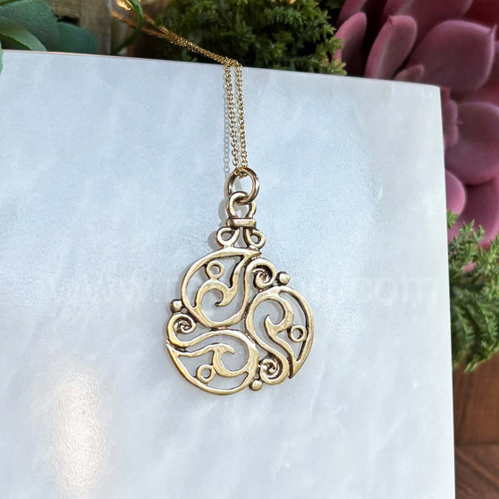 The Inishglora Triskele Pendant features an intricate, openwork circular design based on a traditional triskele motif. Pictured in yellow gold.