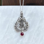 The Lyall Gem Pendant has a central thistle flower, curving side leaves and a 6mm gem at the bottom. Shown with Garnet.