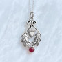 The Flora Gem Pendant features curving oak leaves, a capped acorn and 6mm gemstone. Shown with Garnet.