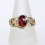 The Elidir Gem Ring features intricate, pierced knotwork with an 8x10mm gemstone. Pictured in yellow gold with Garnet.