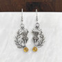 The Cirsium Gem Earrings feature thistle flowers, flanked by a curving leaf on one side, a 6mm gemstone at the bottom and beads and curl accents at the top. Shown with Citrine.