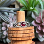 The Hawise Gem Ring features a 6mm gem and pierced curling knotwork. Shown with Garnet.