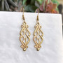 The Fadó Knot Earrings are formed from two overlapping heart shapes with curled ends and large bead accents at the bottom. Shown in yellow gold.