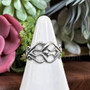 The Fadó Knot Ring is formed from two overlapping heart shapes with curled ends and large bead accent at center.