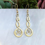 The Grian Triskele Earrings feature a graceful twist drop with a triskele. Shown in 14kt yellow gold.