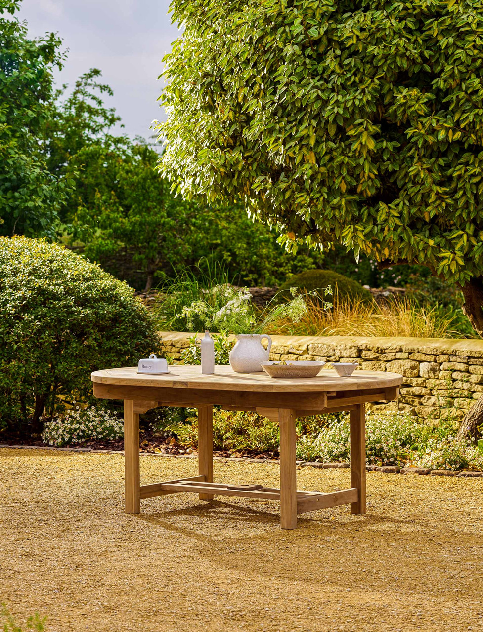 A large oval teak dining table with a slatted top and a parasol hole, shown from above at an angle.