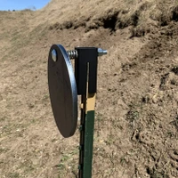Shooter installing hanger onto a steel T-post in dirt range setting, attaching round plate quickly without tools before beginning practice