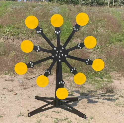 Handgun shooter engaging spinning Texas Star target system in outdoor range, multiple AR500 plates falling sequentially after impact.