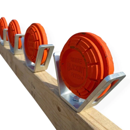 Five-pack clay pigeon holder set mounted on horizontal 2x4 lumber creating rimfire training target system for .22 LR shooting practice at outdoor range