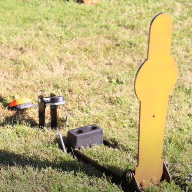 Shooter using clay flipper system on grassy outdoor range, engaging pepper popper target that activates airborne clay pigeon for shotgun training.