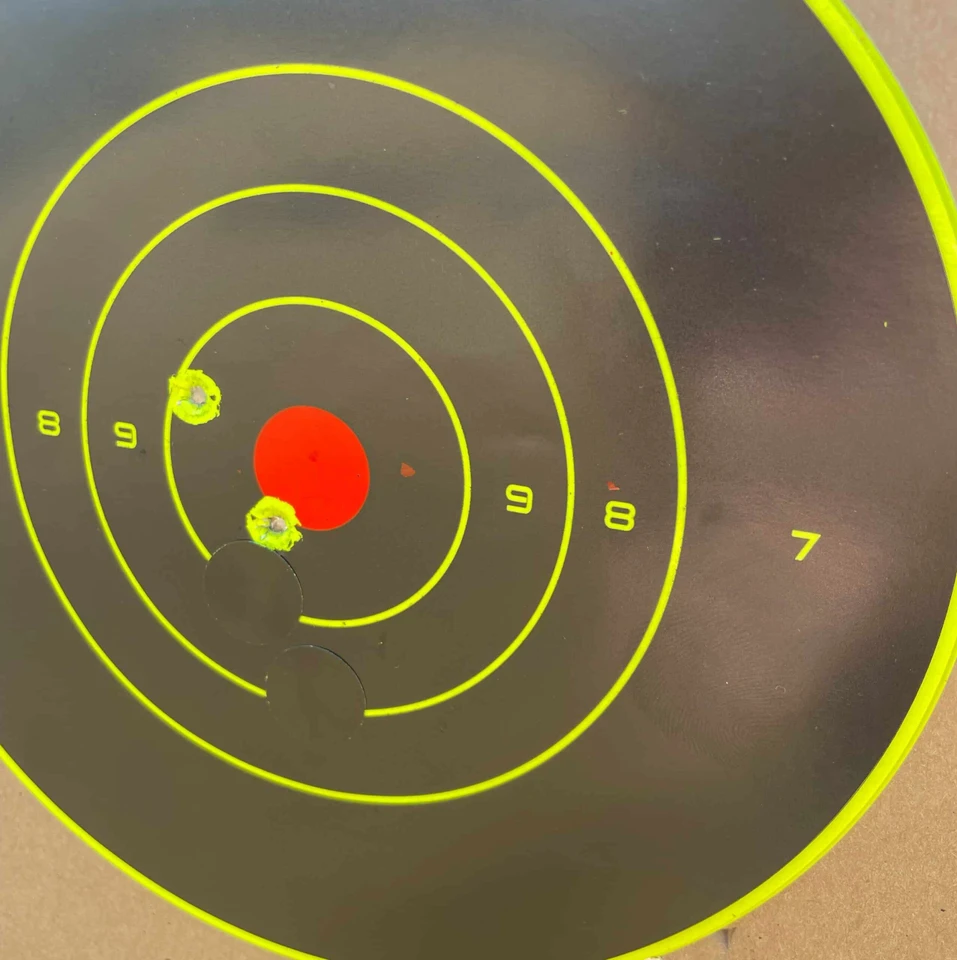 Cardboard target stand outdoors with splatter targets applied, showing multi-zone aiming points used for pistol and rifle accuracy training in daylight shooting range.