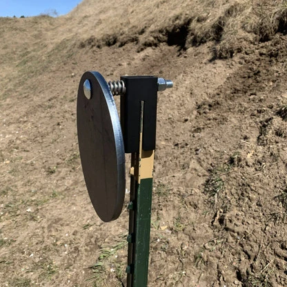 Shooter installing hanger onto a steel T-post in dirt range setting, attaching round plate quickly without tools before beginning practice