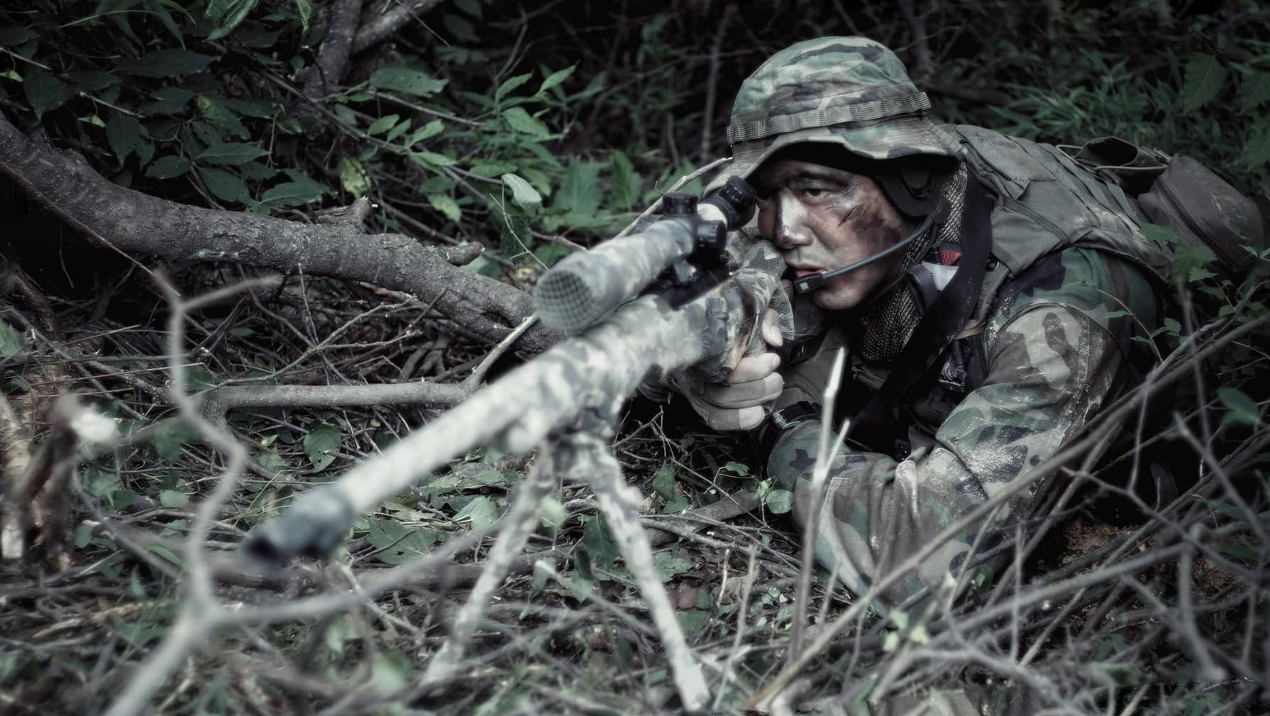 man aiming a camo firearm