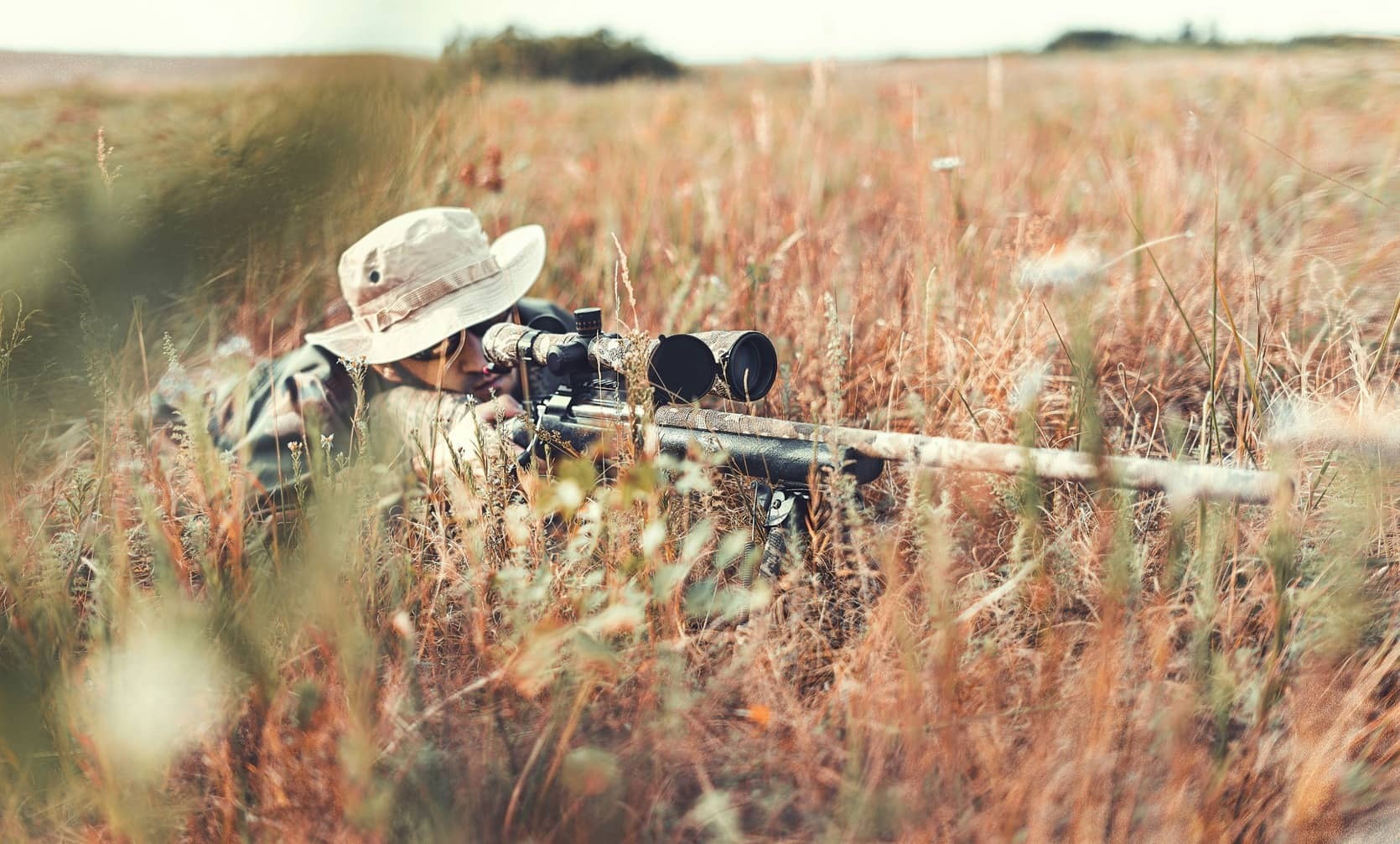 man in tall grass aiming hunting rifle with accessories
