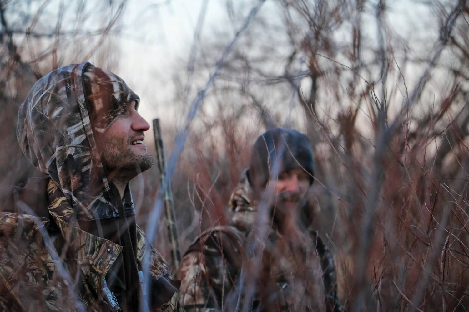 two men wearing camo in woods