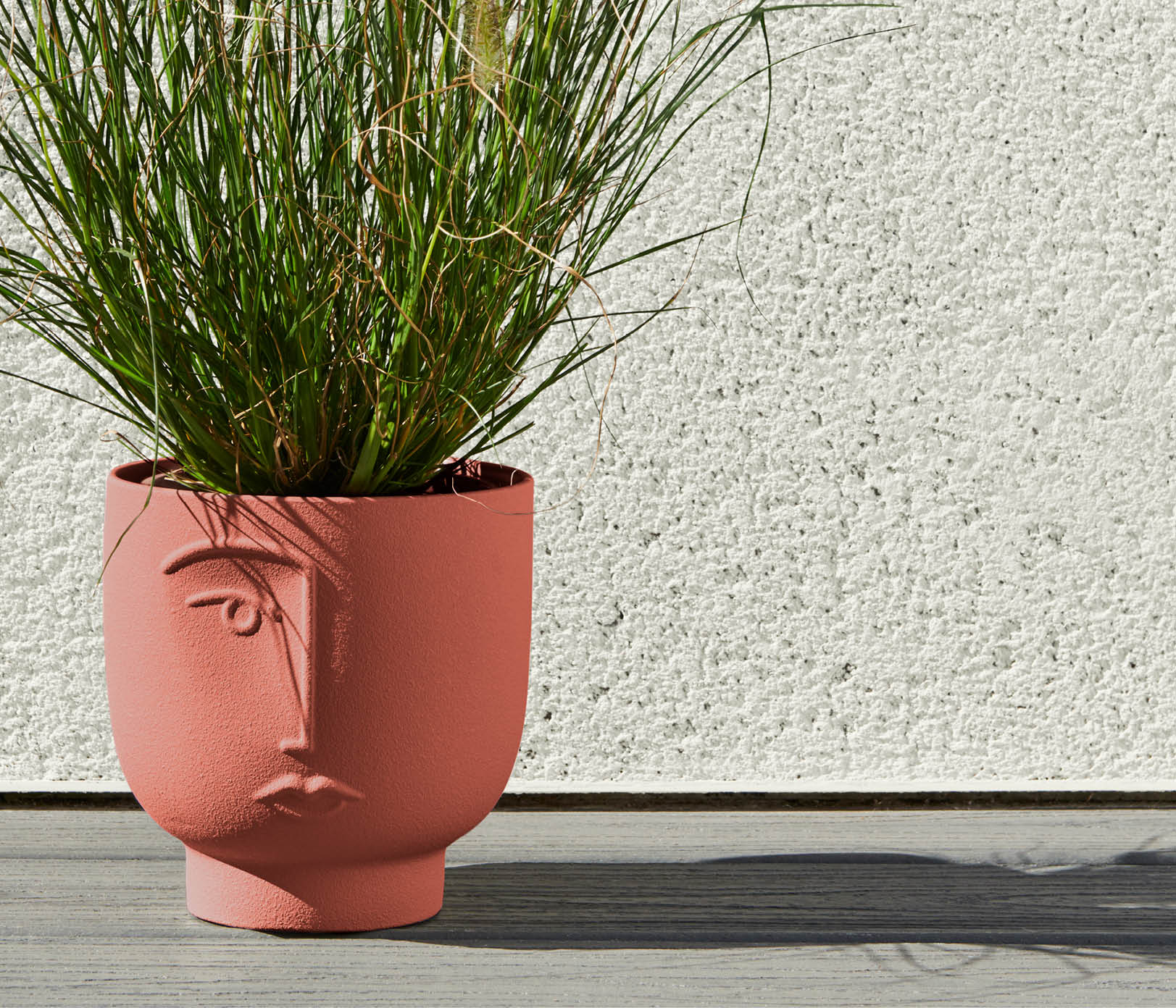 A red plant pot painted in Rust-Oleum colour Fire Brick with a green, grassy plant