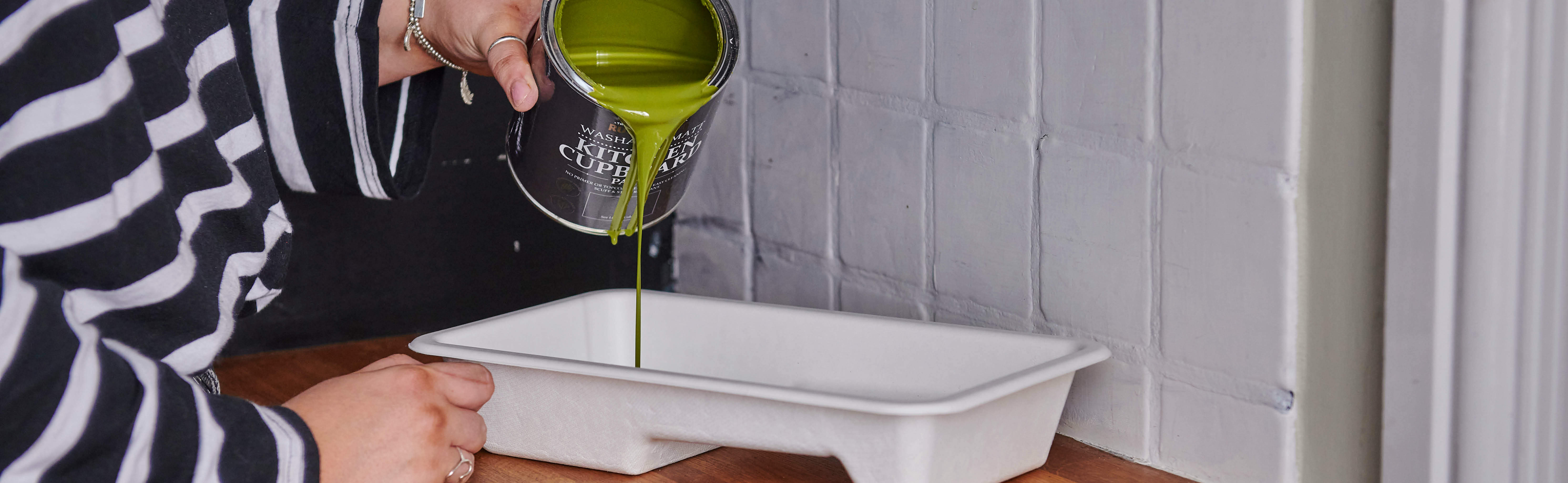 Pouring a can of Kitchen Cupboard Paint into a roller tray. The colour is moss green Jasper.