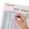 A magnetic calendar planner in pastel colours, featuring a year layout for 2027, with a hand holding a marker.