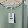 A light green t-shirt hangs on a display, featuring a swing tag with a logo and a label marked "CLOTH."