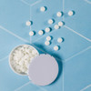 A white mint tin with an open lid and scattered white mints on a blue tiled surface.