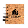 A cork notebook featuring a black spiral binding and the logo for "Twin Peaks Guest House" embossed on the cover.